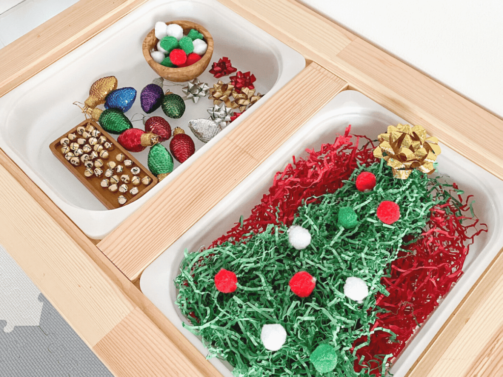 Christmas sensory bin idea using crinkle paper, pompoms ornaments and bows. Have your kids decorate the Christmas tree!